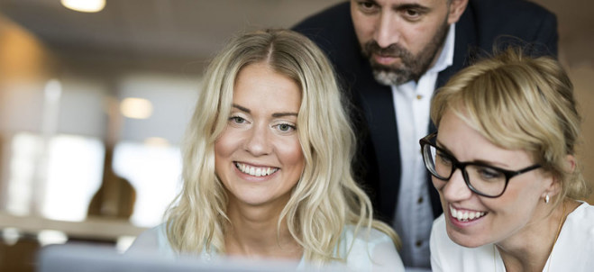Bild på två kvinnor och en man som kollar på en datorskärm. De två kvinnorna ler stort mot skärmen.