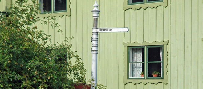 Bild på ett grönt hus på Torekällberget med en skylt framför. På skylten står texten information.