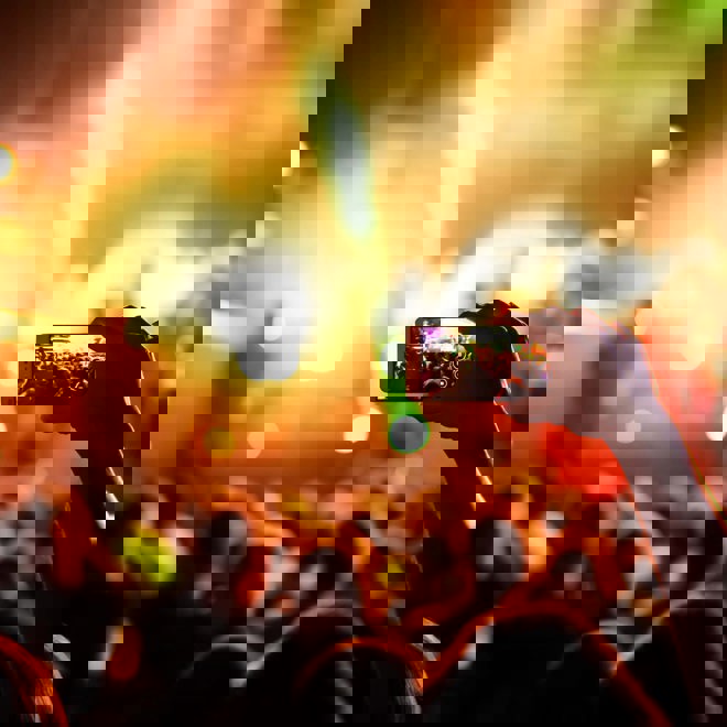 Bild på en hand med en mobiltelefon som spelar in live på en musikfestival.