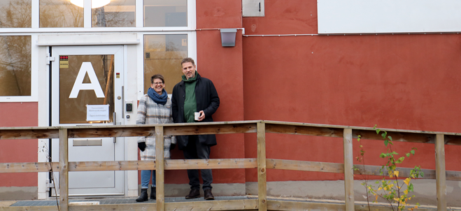 En kvinna och en man utomhus framför en röd byggnad.
