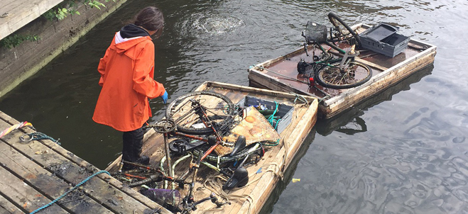 En person står på en brygga och har fiskat upp en hel massa skräp från botten på Maren, exempelvis cykel.