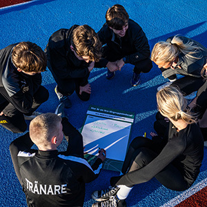 Bild på ungdomar som sitter i ring och tittar ned på ett block.