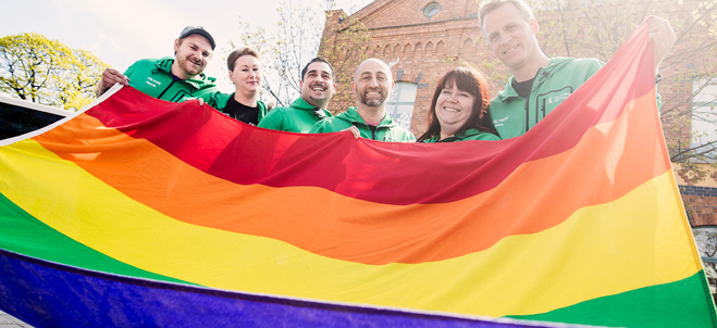 Fotografi på sex fältare som tillsammans håller i en prideflagga.