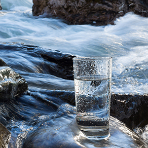 Ett fullt vattenglas på stenar i ett vattendrag får symbolisera infon om vattenskyddsområdet södra Mälaren.