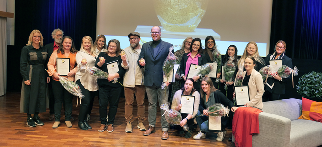 En grupp människor står samlade på en scen. I bakgrunden syns en bild av ett guldäpple.