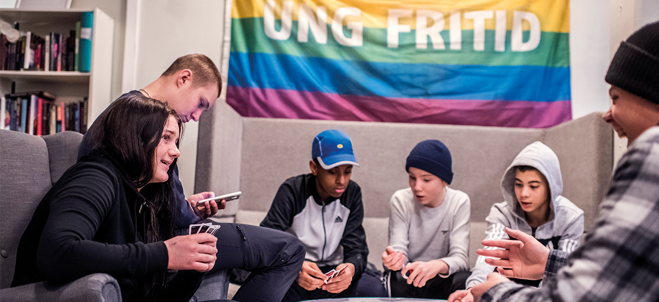 Ungdomar spelar kort framför en regnbågsflagga