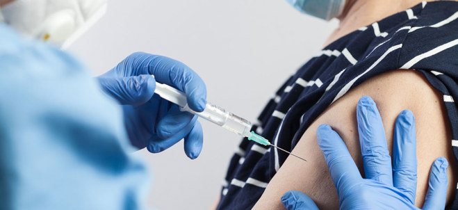 vaccin ges av vårdpersonal med blå handskar till person med uppkavlad ärm