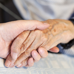 Bilden visar två händer som håller varandra, en äldre och en yngre person.