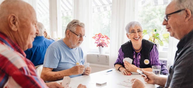 Fyra pensionärer sitter runt ett bord och spelar kort