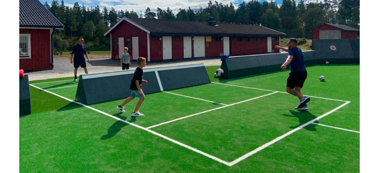 En pojke och en man som spelar fotboll på konstgräs med vita streckade linjer