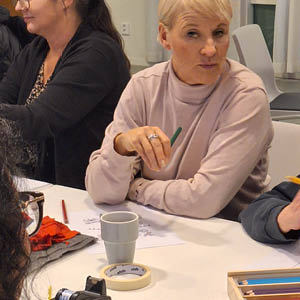 Minister Anna Tenje i rosa tröja pysslar med träffpunktens deltagare vid ett bord