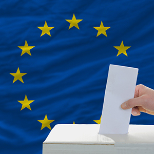 Hand som lägger sin röst i EU-valet framför EU-flaggan.