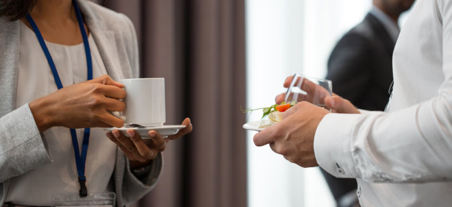 Två personer konverserar medan de står upp och äter frukost