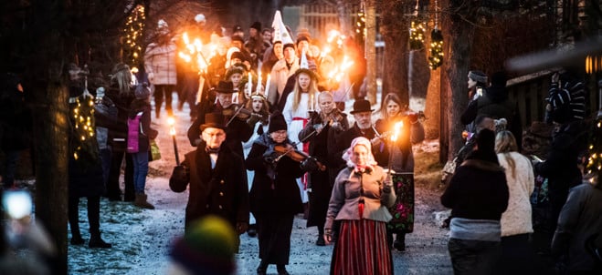 Luciatåg vandrar fram mellan åskådare. Framtill syns stråkspelare.