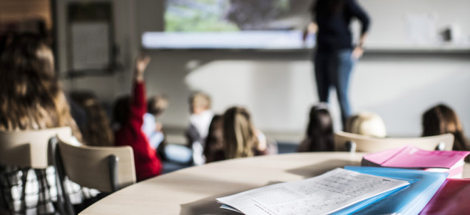 Elever och lärare i klassrum, i förgrunden skolböcker.