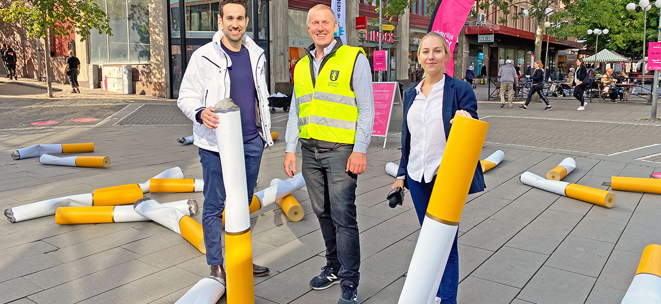 Tre personer som står på gågatan i centrum med stora cigarettfimpar i kartong