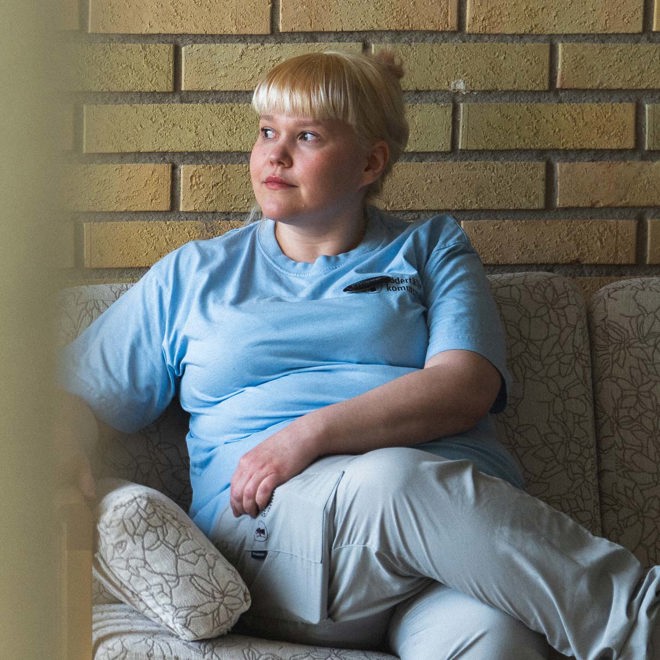 kvinna i blond lugg och ljusblå arbetskläder i en soffa