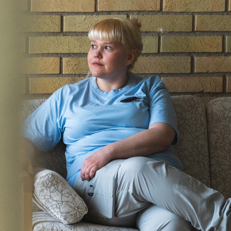 kvinna i blond lugg och ljusblå arbetskläder i en soffa