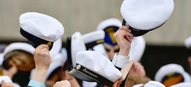 Händer som håller upp studentmössor i luften.