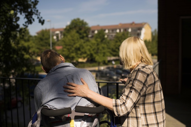 En man i rullstol sitter tillsammans med en personal och tittar ut över en vacker vy