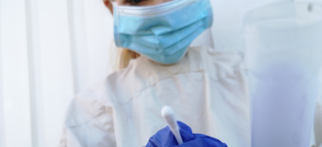 person med skyddskläder och blå handskar med provtagningskit