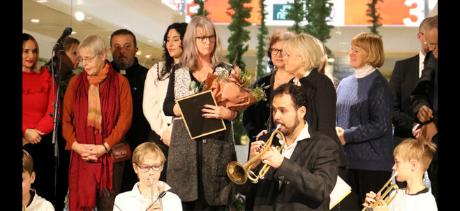 Prisutdelning med flera människor på scen som får blommor, diplom. En trumpetspelande man syns i förgrunden.