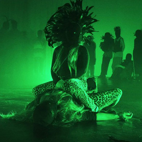 I en dunkel klubbmiljö med grönt ljus sitter en person på en annan
