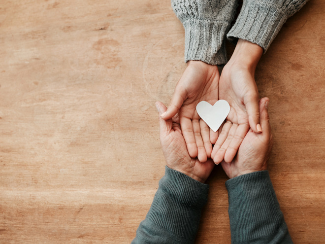 Bild på två händer som vilar i varandra med ett hjärta av papper överst.