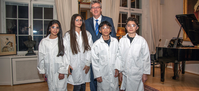 Fyra barn i vita rockar står på rad. Bakom står en man i kostym.