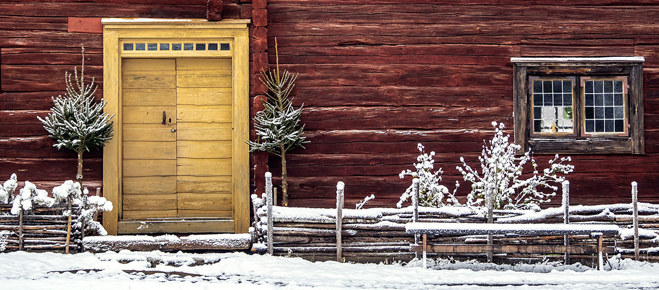Röd husvägg med gul dörr i vinterlandskap.