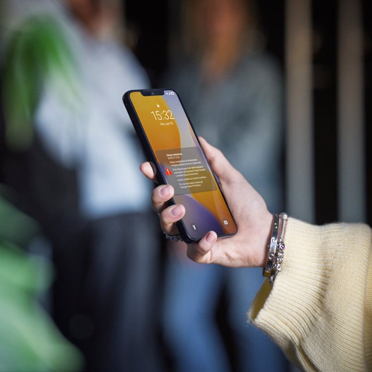 hand håller mobiltelefon med varningstriangel