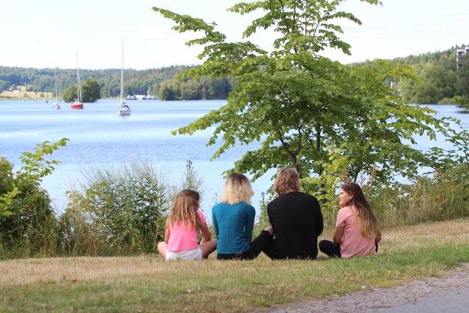 Familj sitter nära vattnet i naturmiljö och konverserar